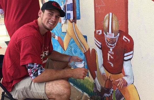 P Bradley Pinion puts the finishing touches on his likeness as part of the “Science of Football” theme of the mural. 